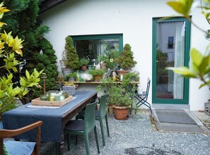 An outdoor patio with a table set for dining, surrounded by potted plants and a variety of decorative items. - Vacation apartment with flair and terrace with a view of the flower and herb garden (Hetzerath)
