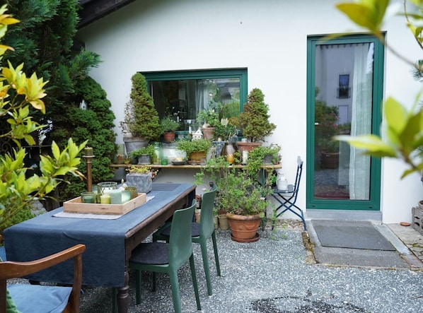 Un patio al aire libre con una mesa lista para comer, rodeado de macetas con plantas y varios objetos decorativos.