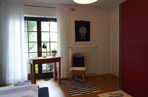A room with a wooden desk, a chair, a radiator, a window with curtains, and a door. - Vacation apartment with flair and terrace with a view of the flower and herb garden (Hetzerath)