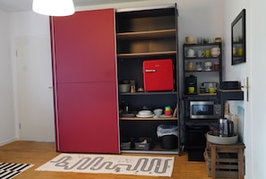 A compact kitchen with a red refrigerator, a microwave, and a coffee maker on the counter.
