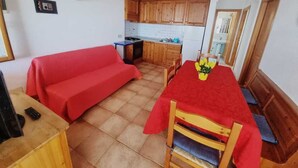 Un espace de vie compact comprenant un coin cuisine, une table à manger avec des chaises et un canapé rouge.