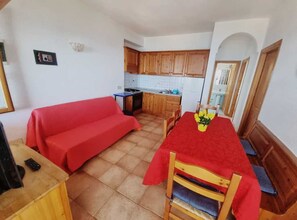 Un espace de vie compact comprenant un coin cuisine, une table à manger avec des chaises et un canapé rouge.