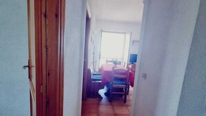 Un couloir avec une porte en bois, un sol carrelé et une arche donnant sur un espace repas comprenant une table et des chaises.