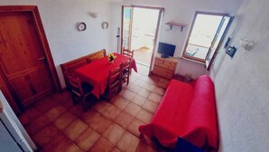 Un espace de vie compact comprenant un coin repas, un canapé, un téléviseur et une porte coulissante donnant sur un espace extérieur.