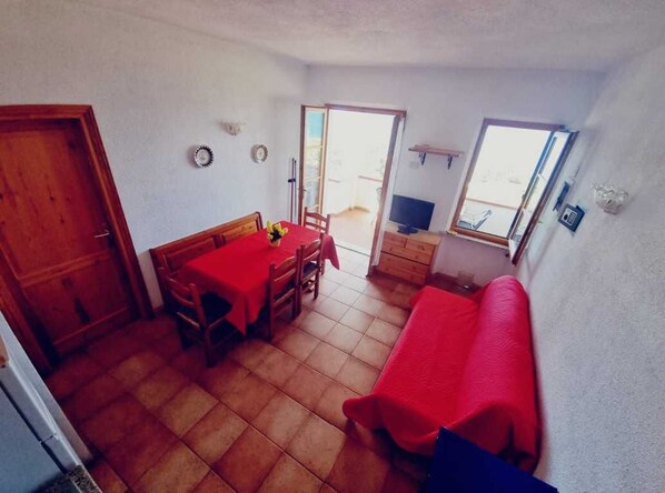 Un espace de vie compact comprenant un coin repas, un canapé, un téléviseur et une porte coulissante donnant sur un espace extérieur.