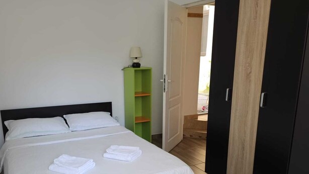 A neatly made bed with white linens, a green shelf unit, a black wardrobe, and a round table with a white tablecloth. - Vivaldi Studios (Cluj-Napoca)
