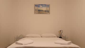 A bedroom with a bed, white linens, a nightstand, a lamp, and a painting of a beach scene.