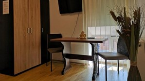 A room with a wooden wardrobe, a television mounted on the wall, a dining table with chairs, and a vase with dried plants. - Vivaldi Studios (Cluj-Napoca)