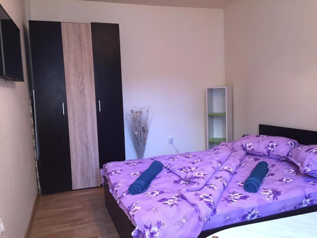 A bedroom with a bed, a wardrobe, a shelf, and a wall-mounted TV.