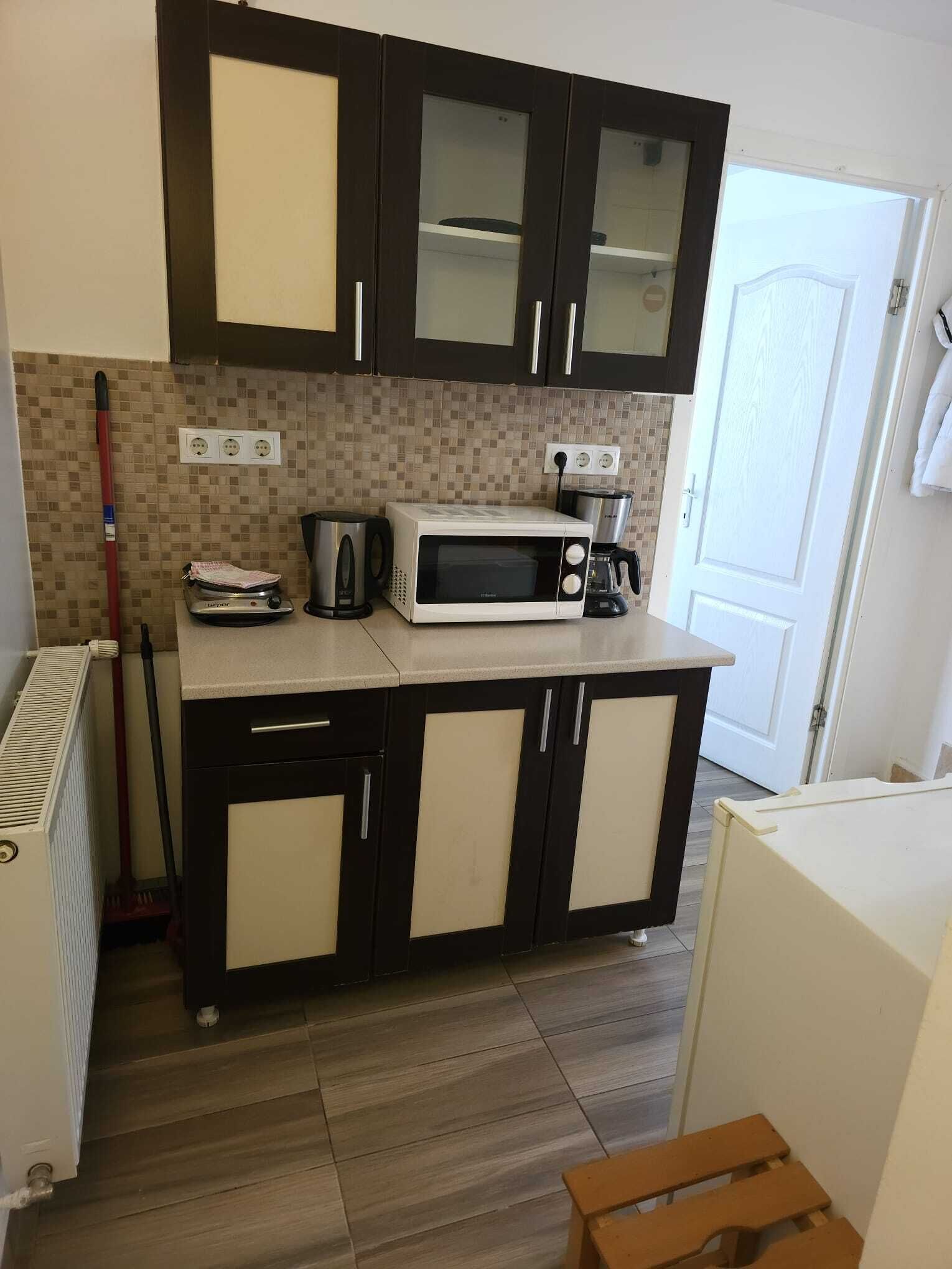 Uma cozinha compacta com armários escuros, micro-ondas, cafeteira e bancada pequena.