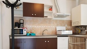 A compact kitchen with dark brown cabinets, a white dishwasher, a coffee maker, and a kettle on the countertop. - Vivaldi Studios (Cluj-Napoca)