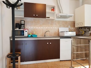 A compact kitchen with dark brown cabinets, a white dishwasher, a coffee maker, and a kettle on the countertop. - Vivaldi Studios (Cluj-Napoca)