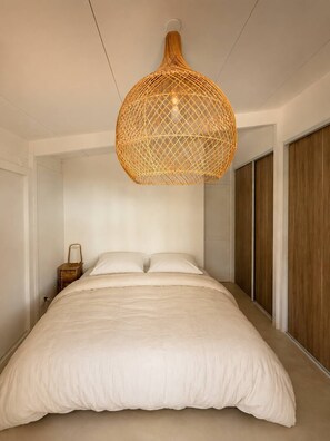 Ein Schlafzimmer mit einem großen Bett, einer hängenden Lampenschirm aus Rattan und Holztüren zu einem Kleiderschrank.