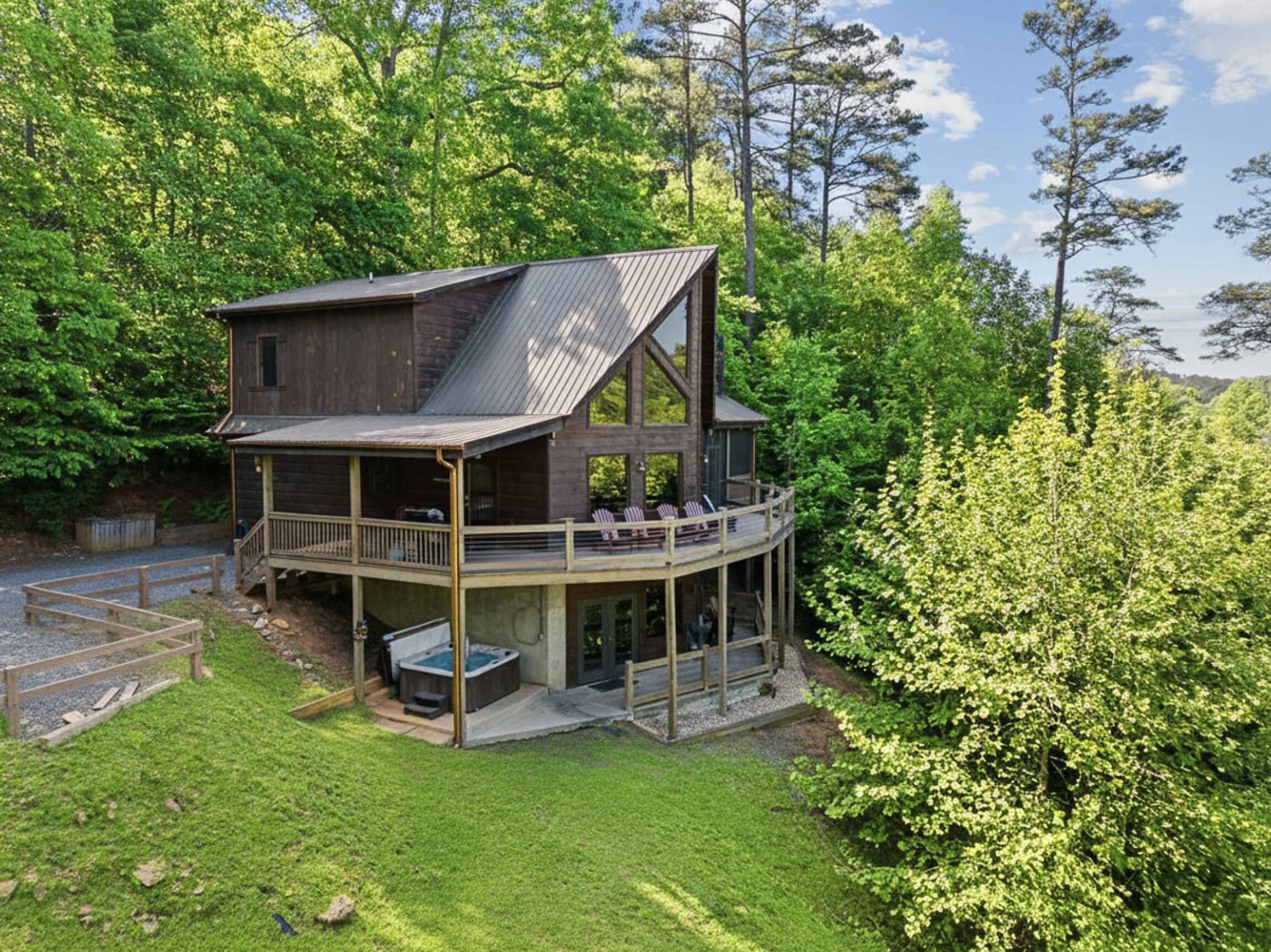 Une cabane dotée d’une terrasse couverte, d’un bain à remous et offrant une vue sur la forêt environnante.