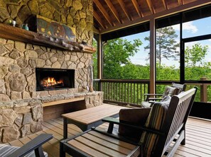 A stone fireplace with a fire, wooden deck seating, and a view of trees. - Mtn Cabin w/ Hot Tub • Game Room • Grill • Views (Blue Ridge)