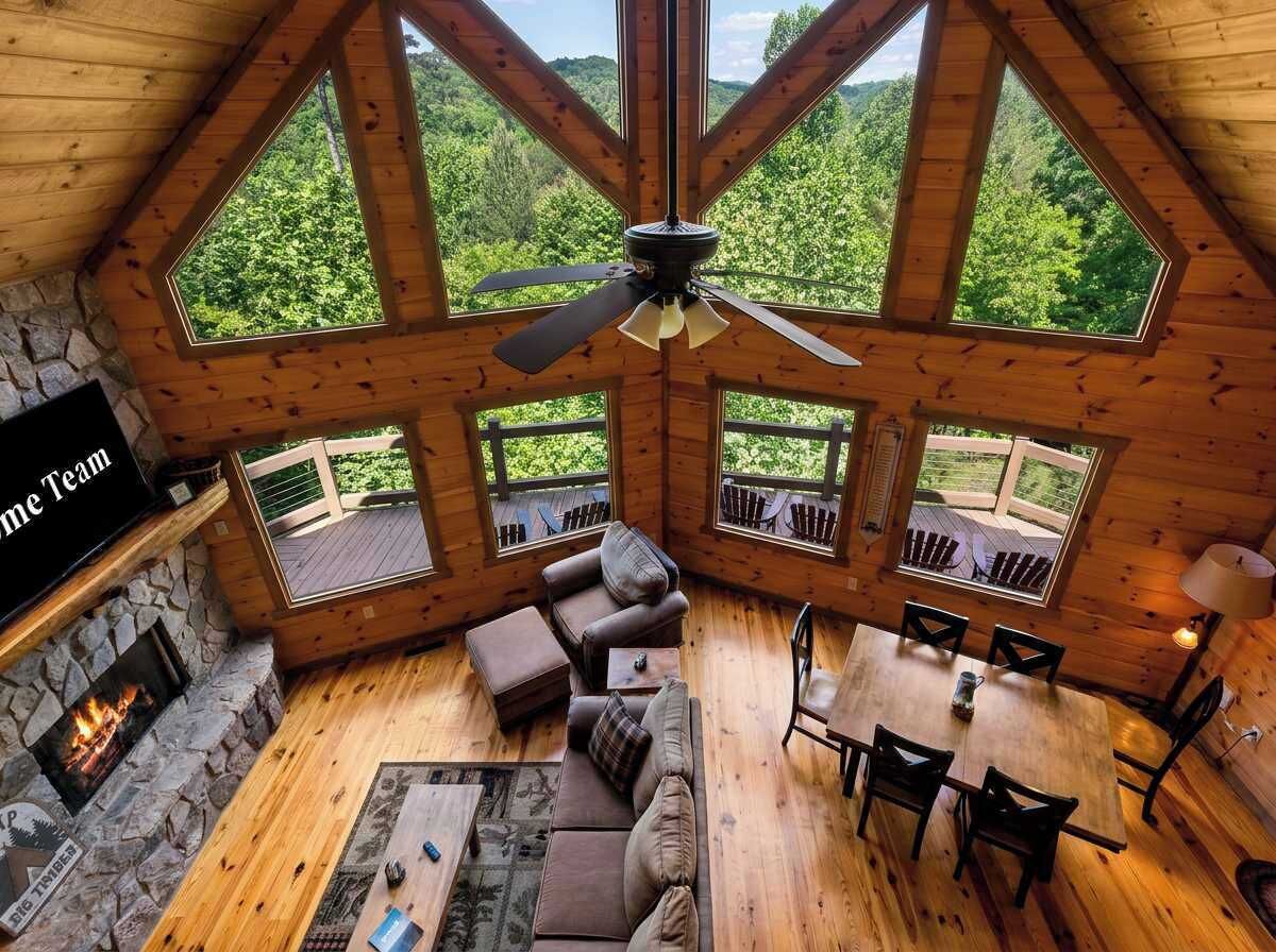 A cabin with a stone fireplace, wooden ceiling, and large windows offering a forest view.