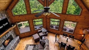 Een chalet met een stenen open haard, houten plafond en grote ramen met uitzicht op een bos.