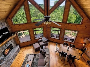 A cabin with a stone fireplace, wooden ceiling, and large windows offering a forest view. - Mtn Cabin w/ Hot Tub • Game Room • Grill • Views (Blue Ridge)