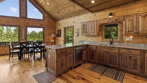 Een houten chalet met een keuken, eethoek en grote ramen.