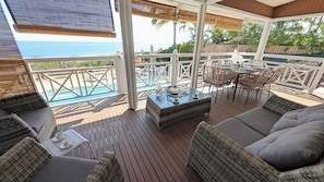 Eine überdachte Terrasse im Freien mit Rattanmöbeln, einem Tisch mit Glasplatte und Blick aufs Meer.