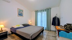 Een hotelkamer met een bed, een nachtkastje met een lamp, een raam met gordijnen en een klein tafeltje met een decoratief object.