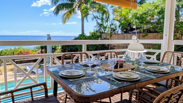 Un coin repas avec une table dressée pour quatre personnes, donnant sur une piscine et l’océan.