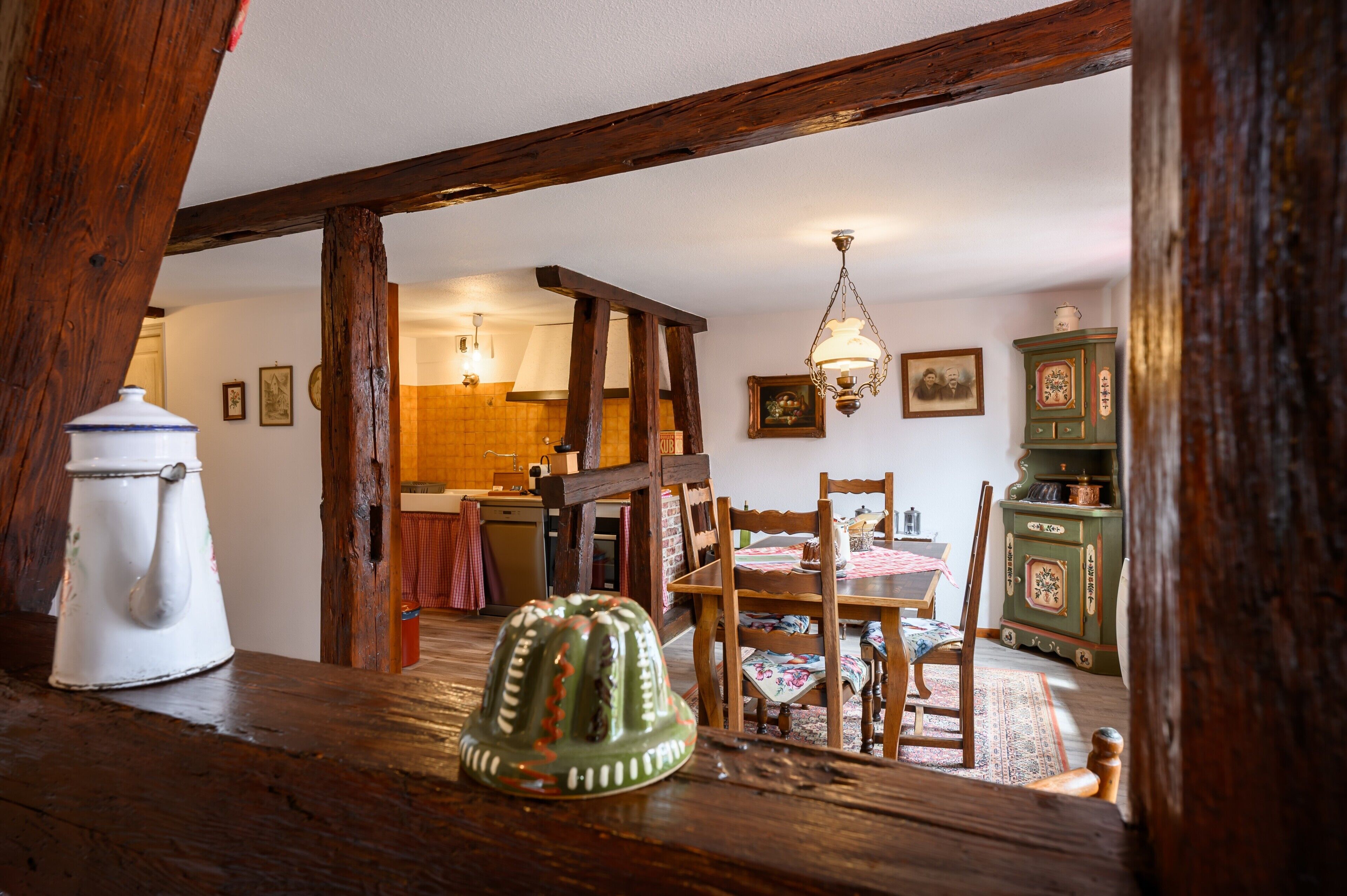 Un coin repas rustique agrémenté de poutres en bois, d’une table en bois, de chaises, d’un lustre et d’une vieille armoire.