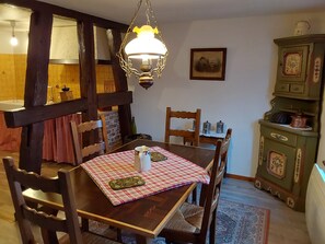 Un comedor con mesa de madera, sillas, mantel a cuadros, lámpara colgante y un aparador antiguo.