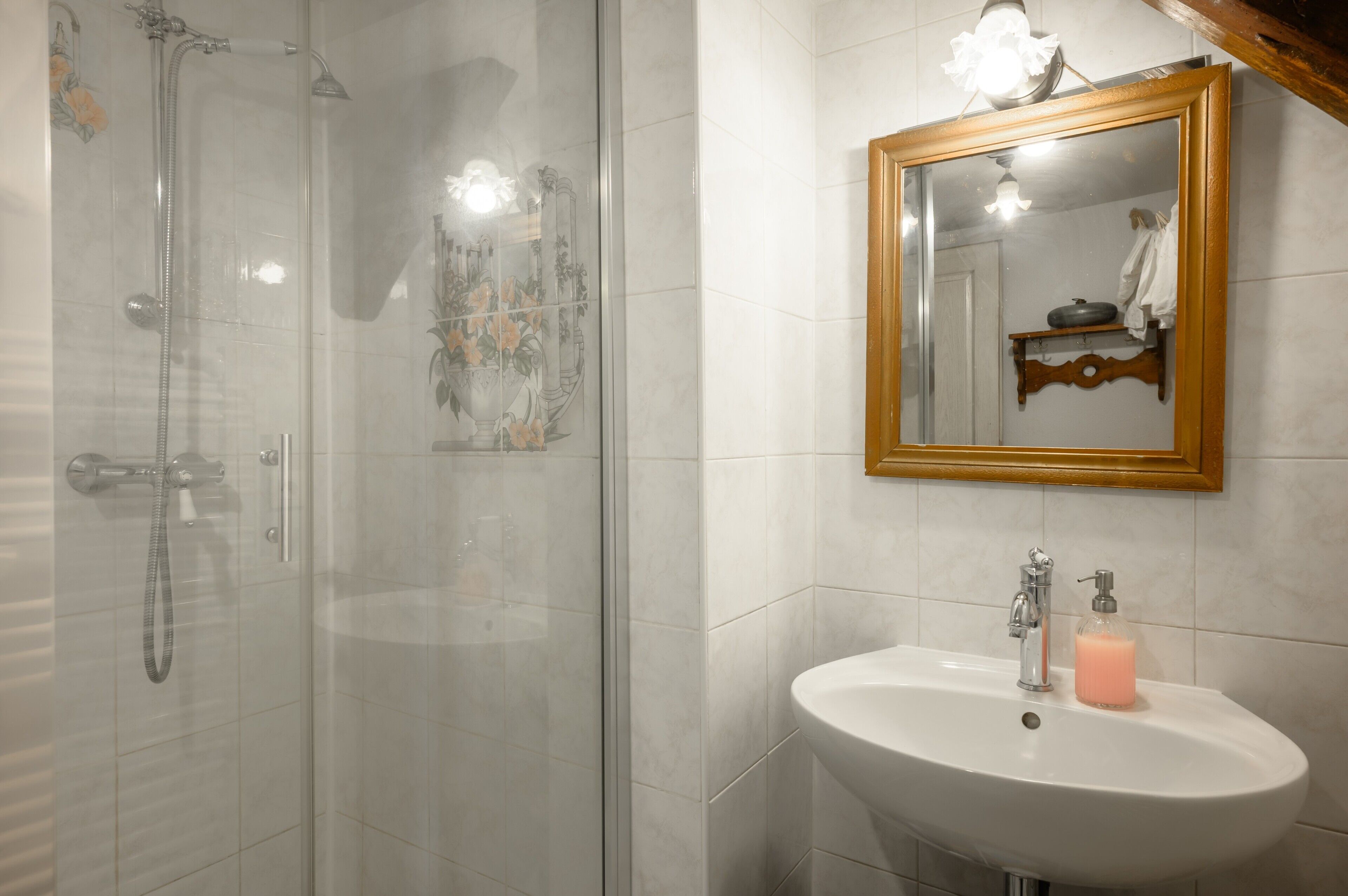 A bathroom with a glass-enclosed shower, a white sink with a soap dispenser, and a wooden-framed mirror.