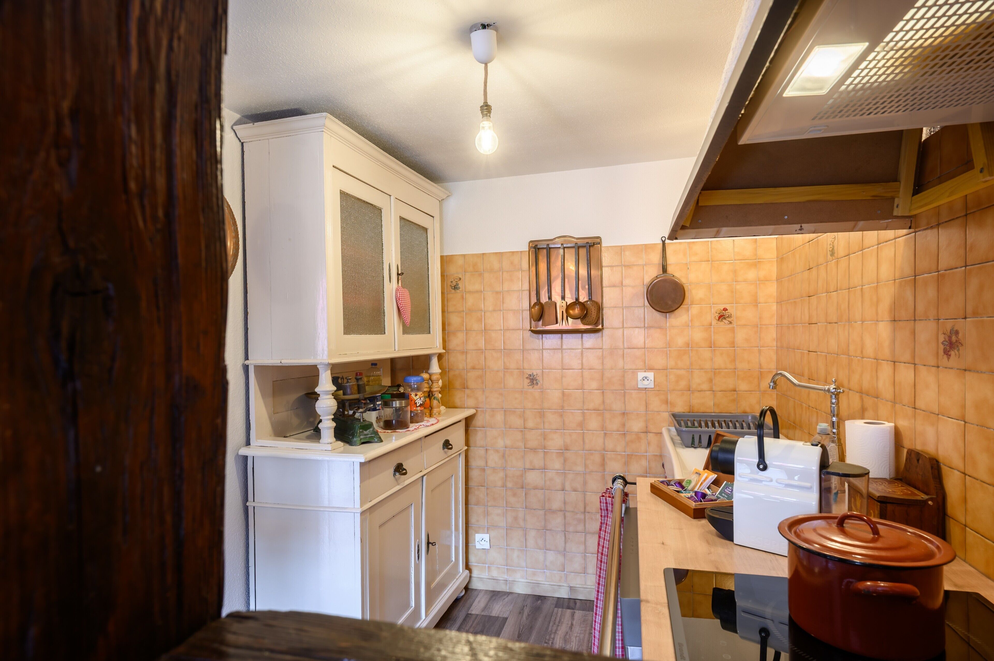 Una cocina con armarios blancos, encimera de madera, una olla roja y un tendedero con utensilios de cocina.