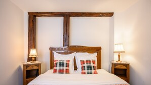 Een bed met een geruit sprei, twee bijpassende kussens, een houten hoofdbord, twee nachtkastjes met lampen en een houten wandstructuur.