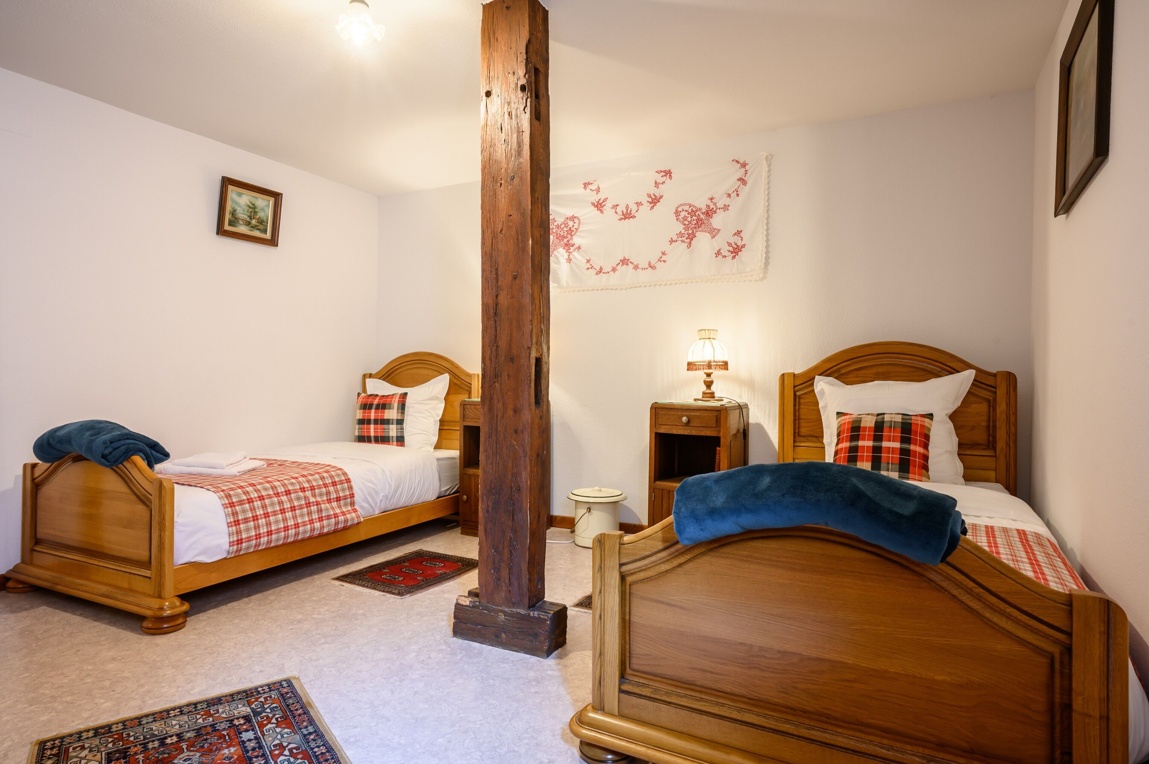A bedroom with two wooden beds, a nightstand, a lamp, a wall tapestry, and a framed picture.
