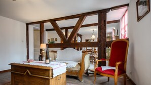 Een kamer met een houten bed, een rode stoel, een houten dressoir en een grote, zichtbare houten balkenconstructie.