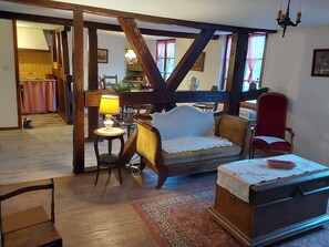 Una habitación tradicional con vigas de madera a la vista, un sofá, una silla, una mesita con una lámpara y un aparador.