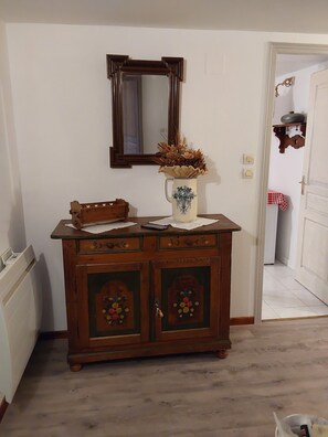 Une commode en bois ornée de motifs floraux sculptés, un miroir au-dessus, et un vase contenant des fleurs séchées.