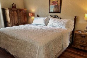 Ein Bett mit weißer Bettdecke, ein Nachttisch aus Holz mit einer Lampe und ein Holzschrank.