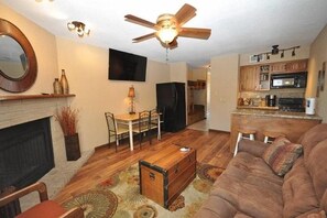 Ein Wohnzimmer mit einer Couch, einem Couchtisch, einem Kamin, einem Essbereich und einer Küche mit Holzschränken und einer Mikrowelle.