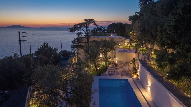 A poolside view of a modern house with a view of the sea at dusk. - Luxury Villa with Private Pool, Capri Views and Panoramic Rooftop (Campania)