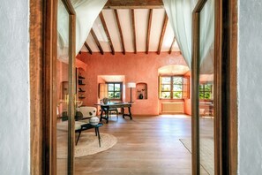 An interior with a wooden floor, a dining table, a sofa, and a window with a view of greenery.