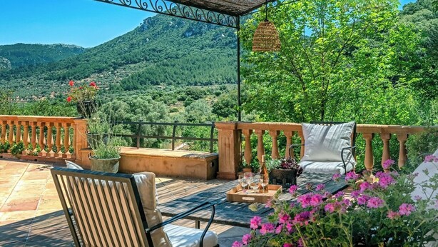 Une terrasse avec une chaise, une table avec des verres et une bouteille, et un luminaire suspendu.