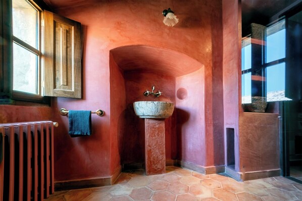Un baño con lavamanos de piedra, un perchero, un radiador y una ventana.