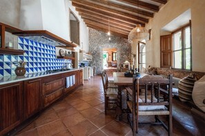 Una cocina rústica con pared de piedra, vigas de madera en el techo y una zona de comedor con mesa y sillas de madera.