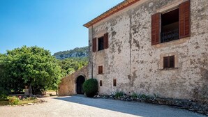 Un bâtiment de style rustique, avec une façade en pierre, des volets en bois et une allée gravillonnée.