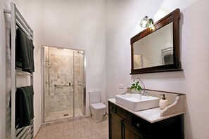 A bathroom with a glass-enclosed shower, a white toilet, a sink with a mirror, and towels on a rack.