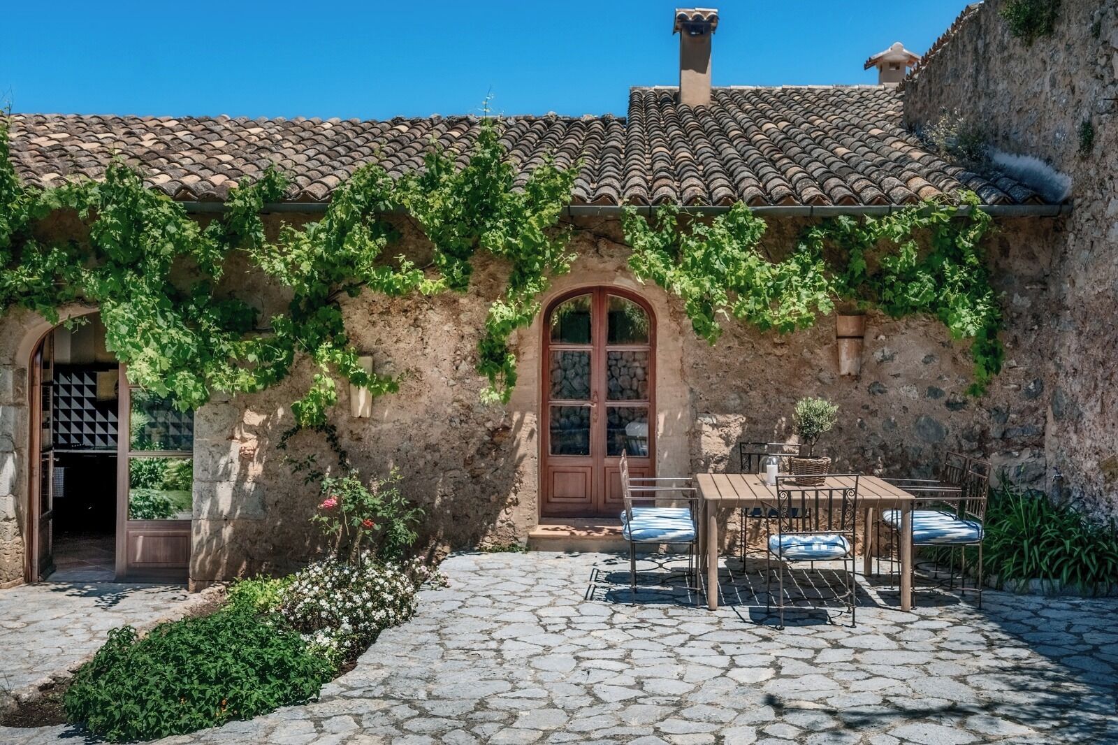 A rustic building with a stone facade, a tiled roof, and a small outdoor seating area with a table and chairs.