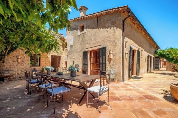 A rustic stone building with a tiled patio, a dining table with chairs, and a small garden area.