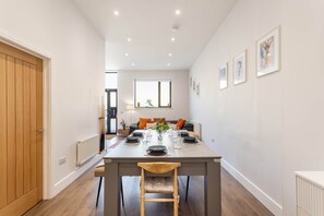 A modern dining area with a wooden table, chairs, and a view into the living room. - Chic 2-Bed Seaside Escape in Vibrant Kemp Town (Brighton and Hove)