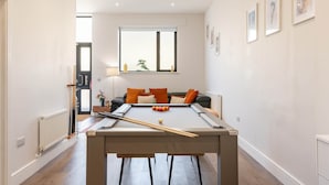 Ein Billardtisch in einem Raum mit einer Couch, einem Fenster und gerahmten Bildern an der Wand.