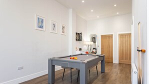 Ein Billardtisch mit Kugeln, eine Lampe und ein Spiegel in einem Raum mit Holzboden und weißen Wänden.