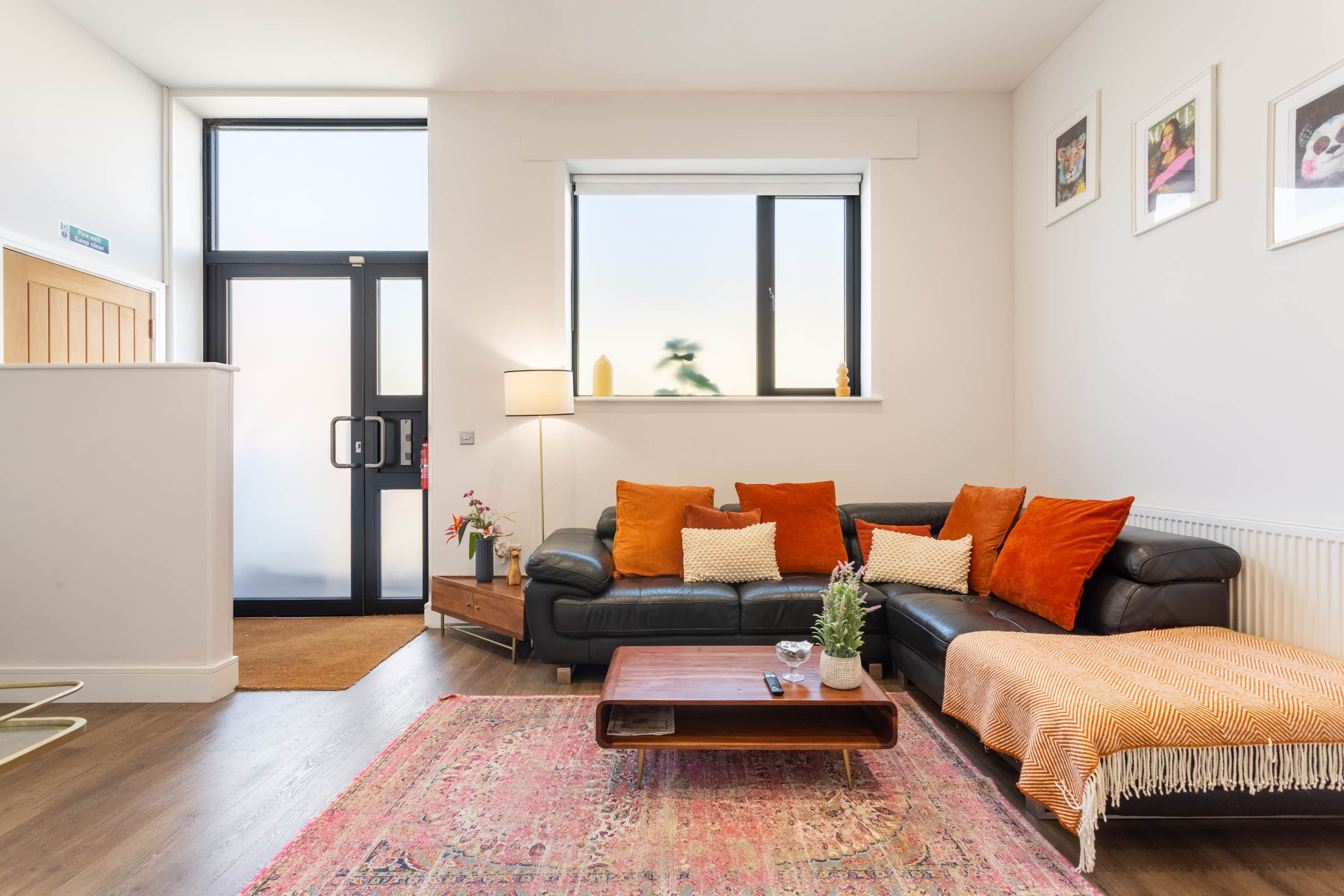 A modern living room with a black leather sofa, a wooden coffee table, and a patterned rug.